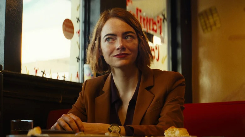 Emma Stone with red hair and lipstick sitting in restaurant in Kinds of Kindness