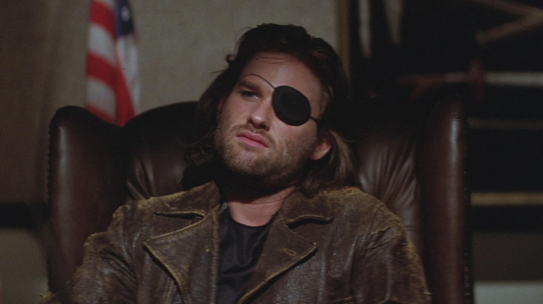 Kurt Russell as Bob "Snake" Plissken, leaning back in a chair in Escape from New York.