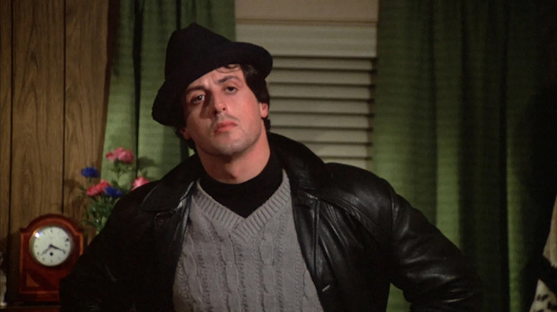 Rocky (Sylvester Stallone) in a sweater, coat, and hat in a living room in Rocky