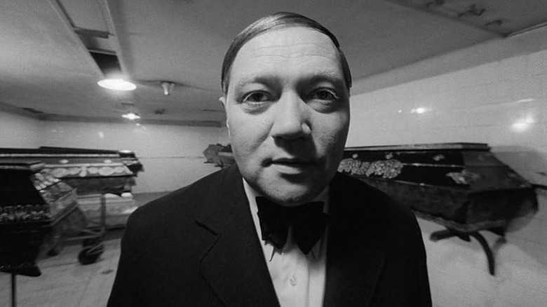 Karel Kopfrkingl (Rudolf Hrušínský) stares into the camera with coffins behind him in The Cremator