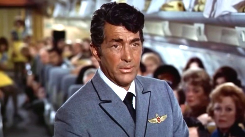 Vernon Demerest (Dean Martin) stands in the middle of an aisle to a full airplane in Airport (1970)