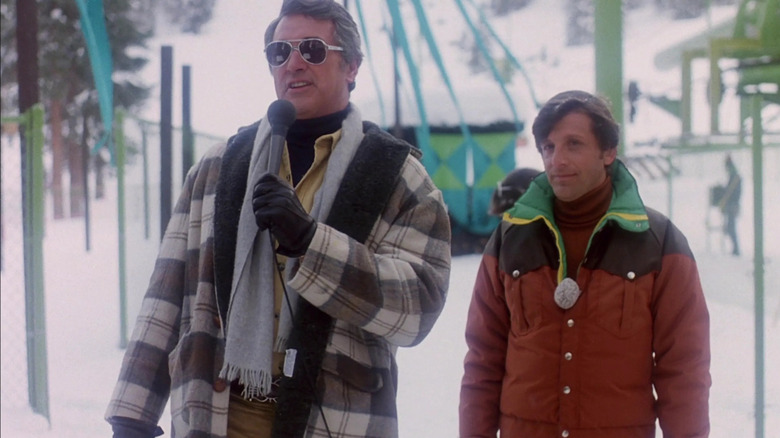 David Shelby (Rock Hudson) speaks into a microphone by a ski lift in Avalanche (1978)