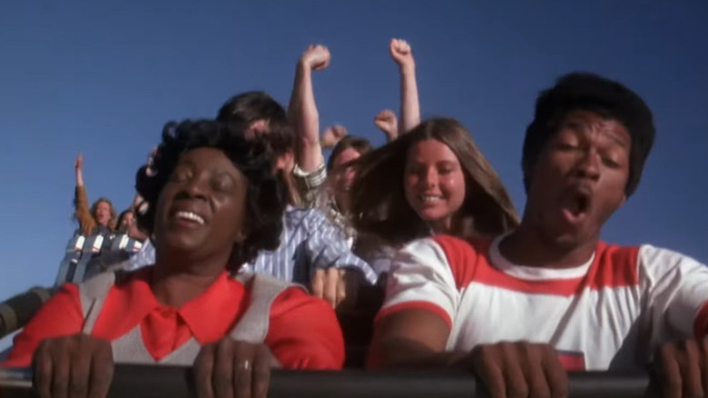 A group of riders happily cheer on a rollercoaster as it descends in Rollercoaster (1977)