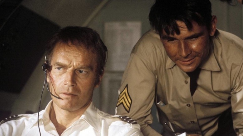 A disheveled Hank O'Hara (Charlton Heston) pilots a plane as Jerome K. Weber (James Brolin) speaks to him over his shoulder in Skyjacked