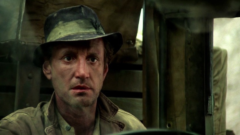 Roy Scheider as Jackie Scanlon in Sorcerer, with a dirty face and clothes as he sits in a truck.