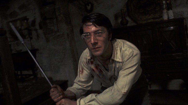 Dustin Hoffman as David Sumner in Straw Dogs, looking sweaty and disheveled while wielding a cane as a weapon.