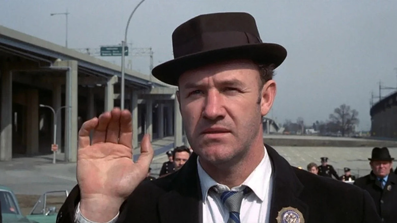 Gene Hackman as "Popeye" Doyle in The French Connection, raising his right hand with other cops and detectives behind him.