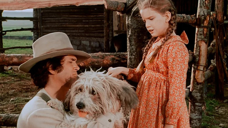 Charles Ingalls (Michael Landon) holds a dog while Laura Ingalls (Melissa Gilbert) watches in Little House on the Prairie