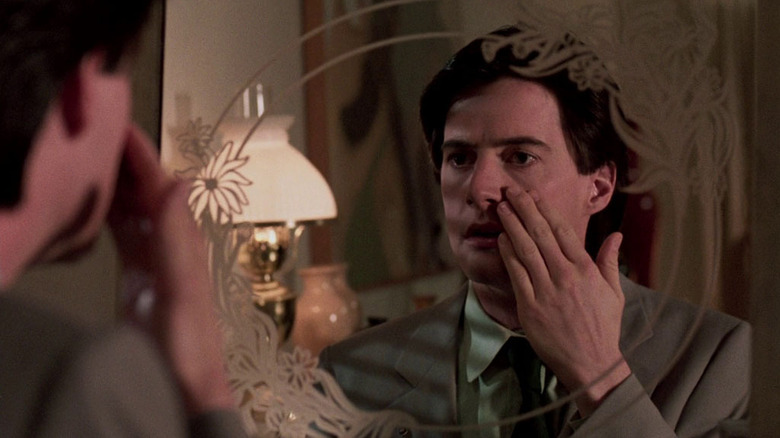 Kyle MacLachlan as Lloyd Gallagher in The Hidden, staring into a mirror and touching his face with concern.
