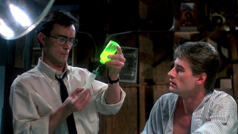 Herbert West (Jeffrey Combs) fills a syringe with a glowing green liquid as Dan Cain (Bruce Abbott) watches in Re-Animator