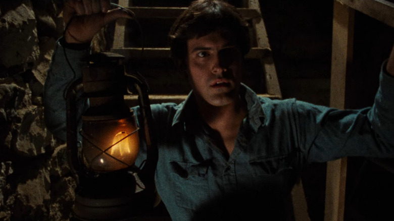 Ash Williams (Bruce Campbell) holds a lantern while descending into a cellar in The Evil Dead