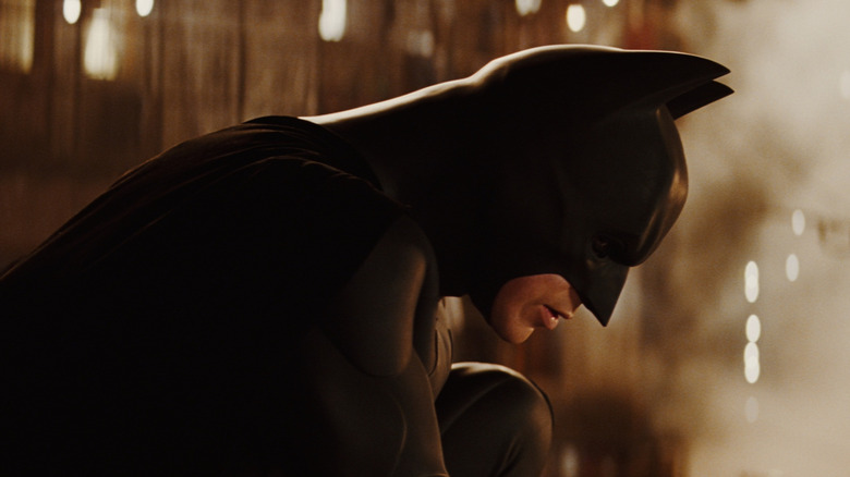 Christian Bale as Bruce Wayne/Batman in Batman Begins, perched in his Batsuit in a profile shot.