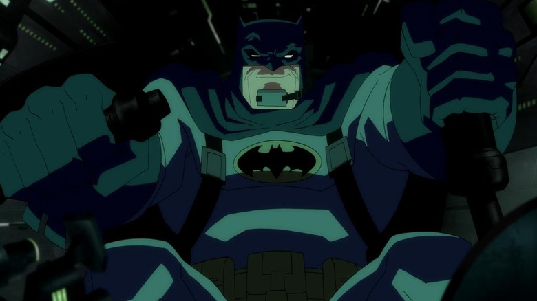 Batman (voiced by Peter Weller) in Batman: The Dark Knight Returns, Part 1, in the Batmobile cockpit, smirking and driving the vehicle.