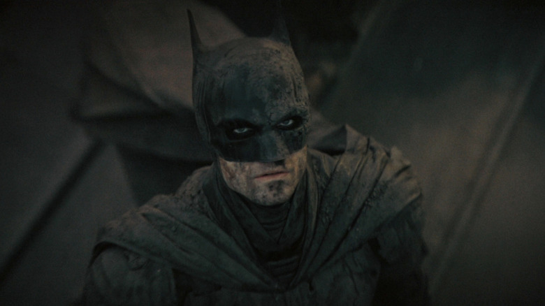 Robert Pattinson as Bruce Wayne/Batman in The Batman, standing and looking up, covered in mud
