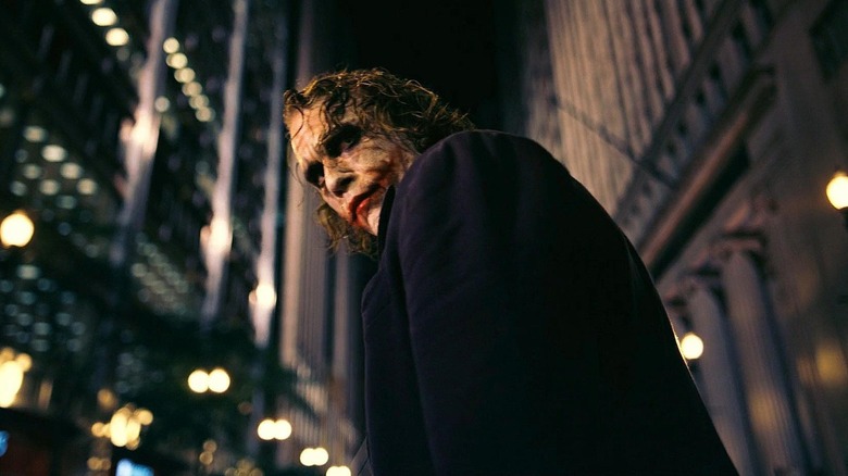 Heath Ledger as The Joker in The Dark Knight, turned and looking over his shoulder on the city streets.