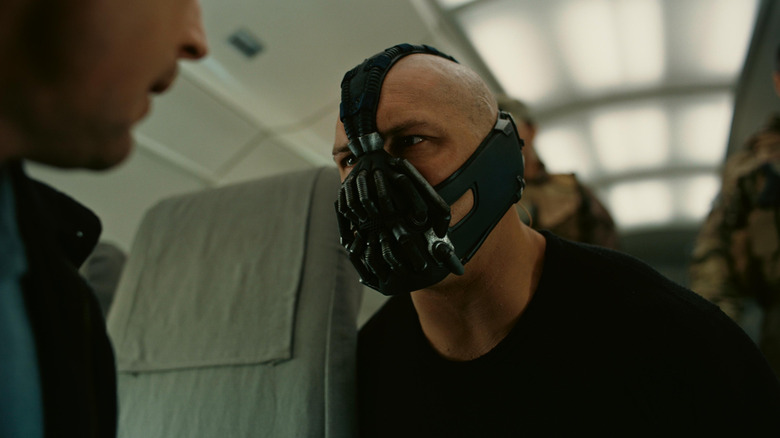 Tom Hardy as Bane in The Dark Knight Rises, kneeling down in front of someone with soldiers behind him, mask on.