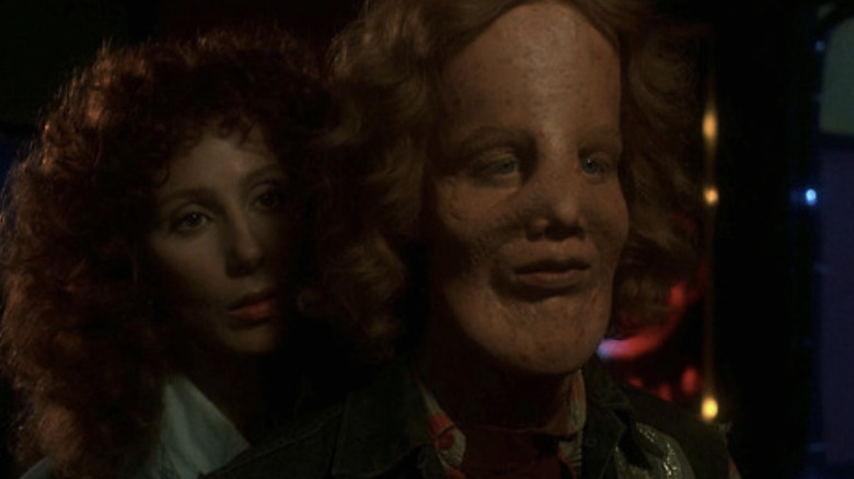 Cher as Florence "Rusty" Dennis standing behind Eric Stoltz as Roy L. "Rocky" Dennis as they look at his face in a funhouse mirror in Mask