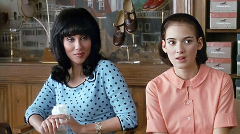 Cher as Rachel Flax wearing a blue dress with black polka dots sitting next to Winona Ryder as Charlotte Flax wearing a peach dress in a show store in Mermaids