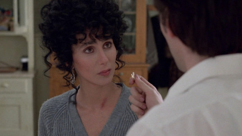 Cher as Loretta Castorini standing in her kitchen with her hair up as Nicolas Cage as Ronny Cammareri holds up his brother's ring to propose in Moonstruck
