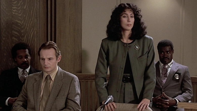 Cher as Kathleen Riley standing in a courtroom wearing green while she defends Liam Neeson as Carl Wayne Anderson who it sitting down and wearing a tie in Suspect