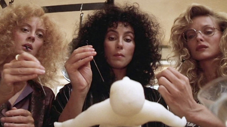 Susan Sarandon as Jane Spofford, Cher as Alexandra Medford, and Michelle Pfeiffer as Sukie Ridgemont holding needles and getting ready to poke a voodoo doll in The Witches of Eastwick