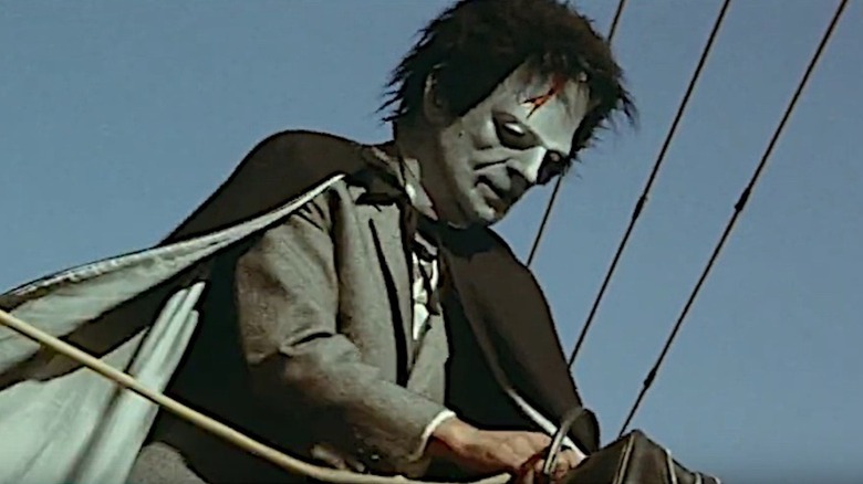 A man wearing a black cape and Frankenstein mask holds a bag in Violent Streets