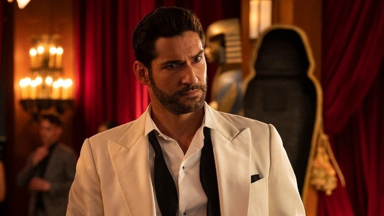 Tom Ellis as Lucifer in white suit with red curtains behind him in Lucifer