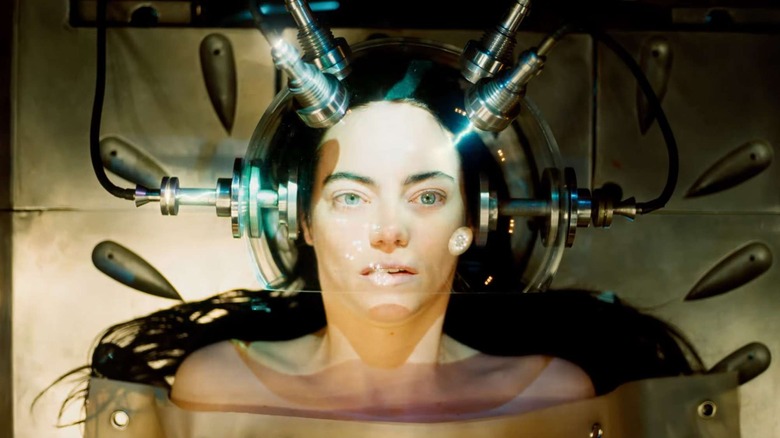 Emma Stone laying down and hooked up to a glass and metal machine as Bella Baxter in Poor Things