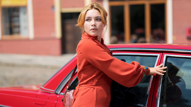 Florence Pugh as Charmian Ross looking over her shoulder in red next to a red car in The Little Drummer Girl