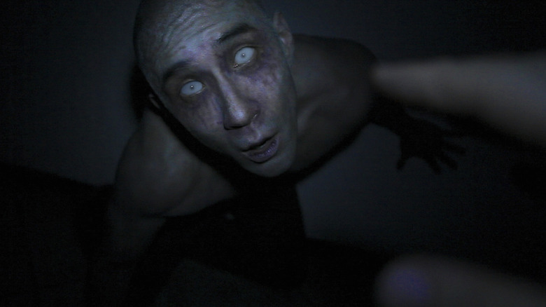 Derek Lee as Derek in Afflicted, seen approaching in the shine of the camera's flashlight, with a pallid face and all blue, glowing eyes.