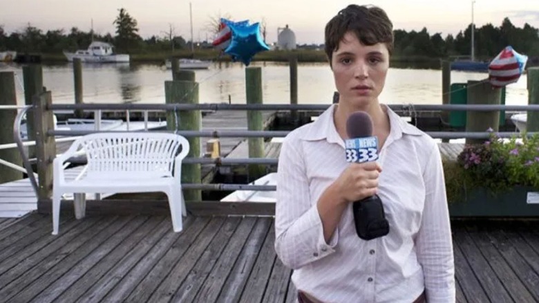 Kether Donohue as Donna Thompson in The Bay, standing in front of a lake with her news microphone as she looks at the camera to give a report.