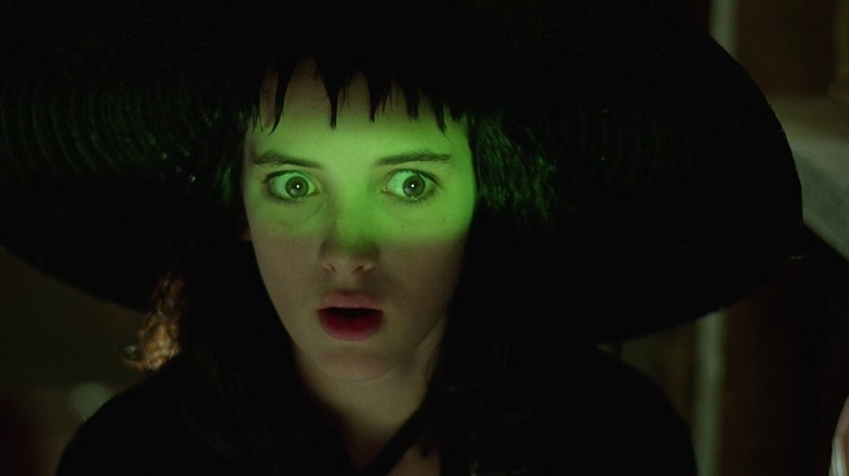 Winona Ryder as Lydia Deetz in Beetlejuice, her face lit with green light as she looks at whatever is emanating it with shock.