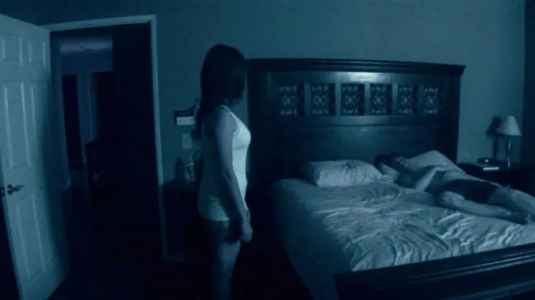 Katie Featherson as Katie and Micha Sloat as Micah in Paranormal Activity, as Katie ominously stands next to the bed looking at Micah sleeping.