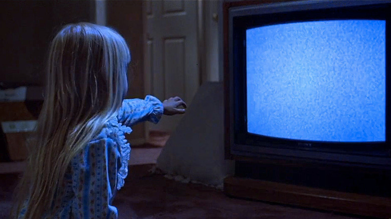 Heather O'Rourke as Carol Anne Freeling in Poltergeist, sitting in front of the static-filled TV and reaching her hand out towards it.