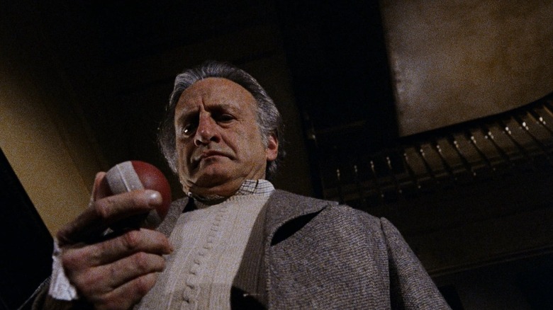 George C. Scott as John Russell in The Changeling, seen at a low angle and looking down at a ball held in his hand.