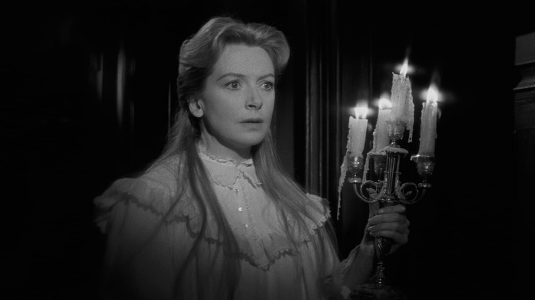 Deborah Kerr as Miss Giddens in The Innocents, lighting the dark with a candelabra and looking on.