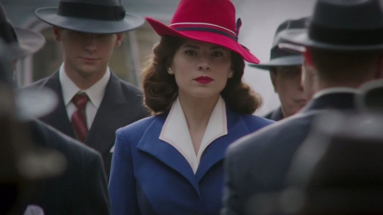 Hayley Atwell as Peggy, wearing a red hat and surrounded by men in suits in Agent Carter