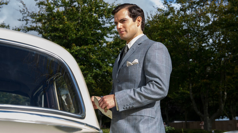 Henry Cavill as Napoleon Solo standing next to a car holding a card in The Man from U.N.C.L.E