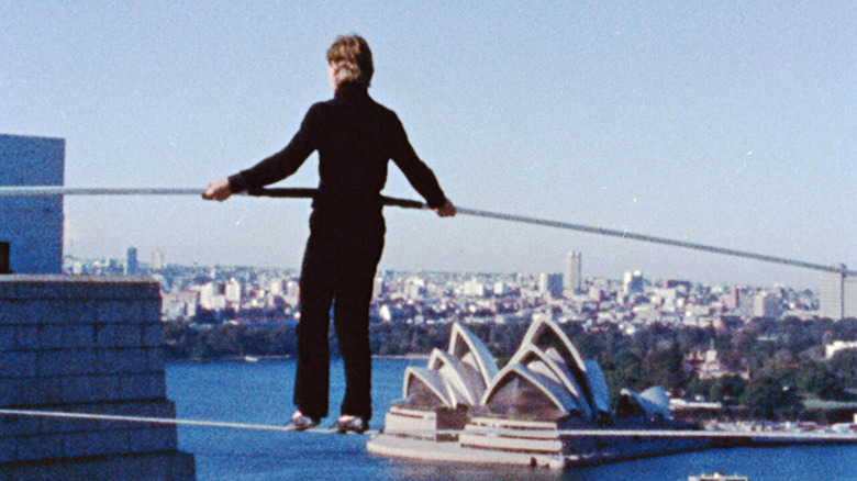 Philippe Petit walks on a wire holding a balancing pole overlooking Sydney Harbor in Man on Wire