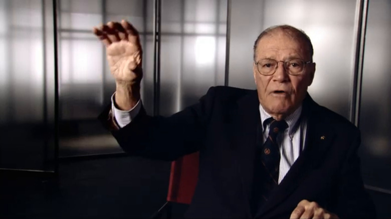 An older Robert McNamara raises his right hand while speaking in The Fog of War