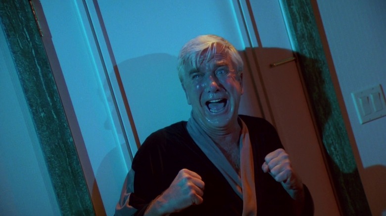 Leslie Nielsen as Richard Vickers in Creepshow, framed in a dutch angle as he stands against a door in a house, cowering in terror as he screams.