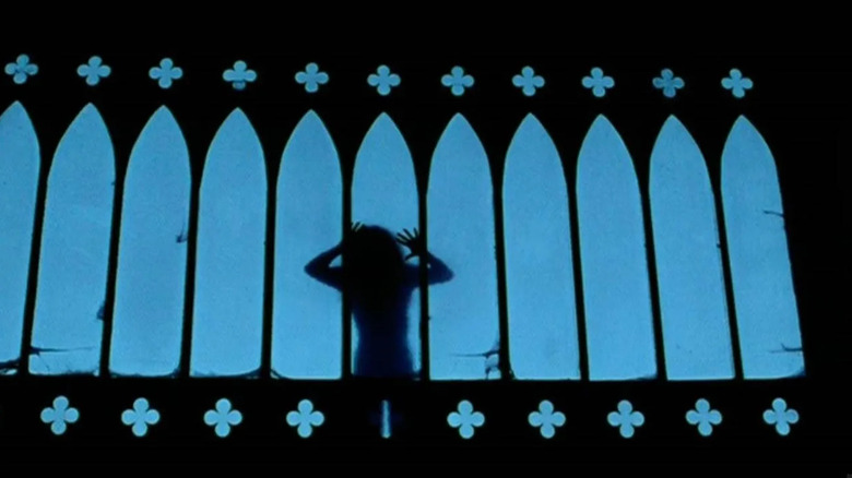 The silhouette of someone in Messiah of Evil, seen through some dramatic church-style windows as the person puts their hands up on the window.