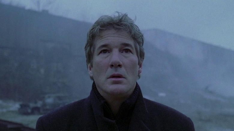 Richard Gere as John Klein in The Mothman Prophecies, standing against a frigid, foggy backdrop and looking on at something in apprehension.