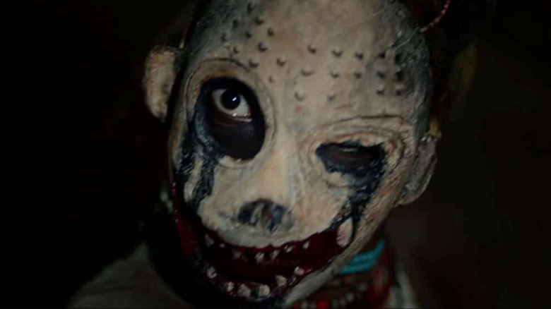 Malaika Abigaba as Nyagak, peering through a mask in His House