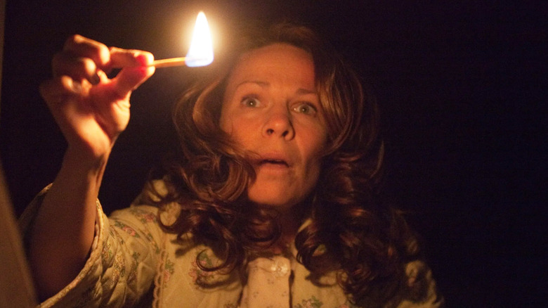 Lili Taylor as Carolyn, holding a match to light a dark room in The Conjuring