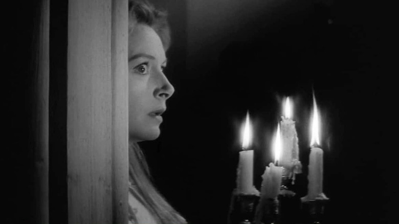 Deborah Kerr as Miss Giddens, looking scared as she rounds a corner, holding a candelabra.