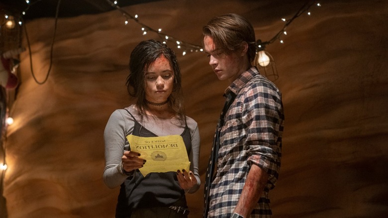 Jenna Ortega as Phoebe Atwell and Judah Lewis as Cole Johnson reading a paper in The Babysitter: Killer Queen