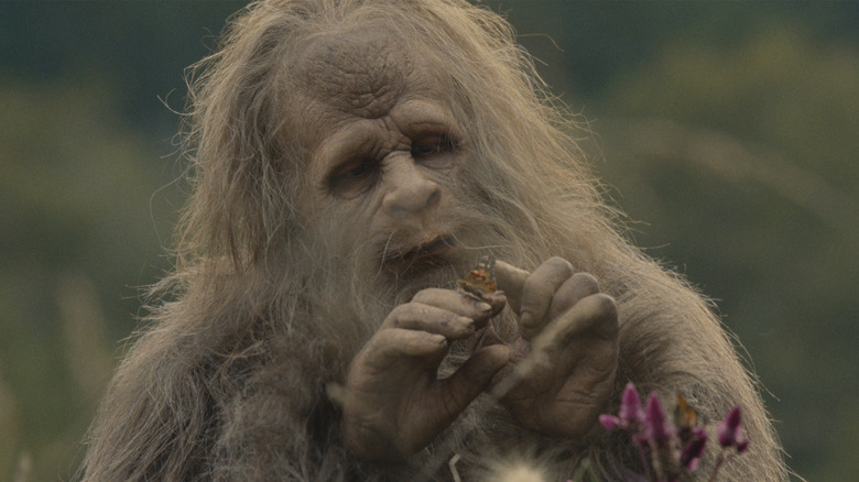 Jesse Eisenberg as a sasquatch looking at and touching a butterfly resting on his finger in Sasquatch Sunset