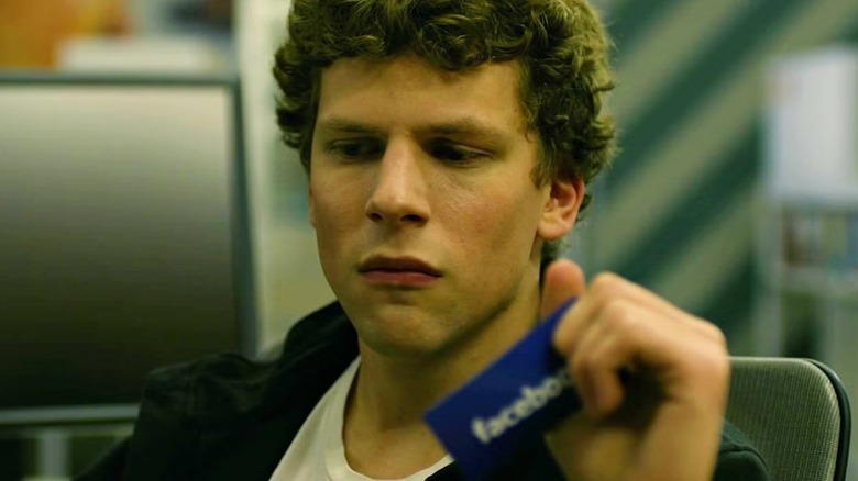 Jesse Eisenberg as Mark Zuckerberg looking down sadly and holding a Facebook business card in his hand in The Social Network