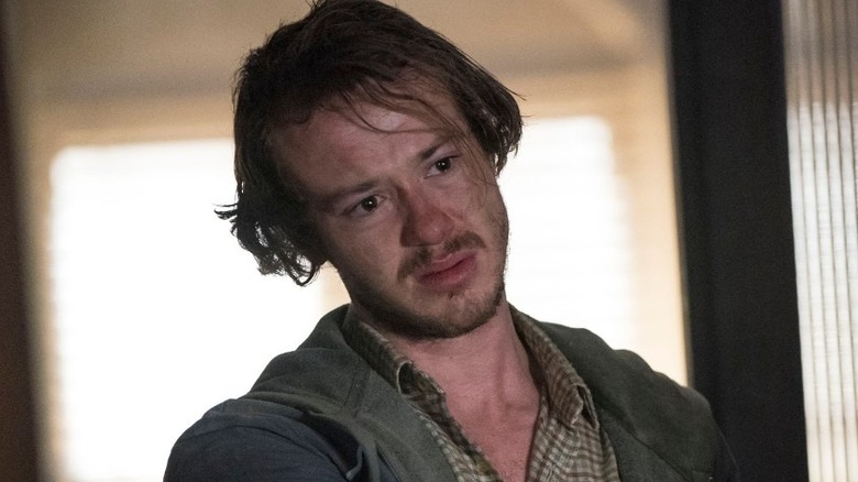 Joseph Quinn as Billy Knight, standing in a doorway on Strike